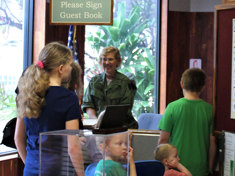 A smiling woman and children gathering around guest book.